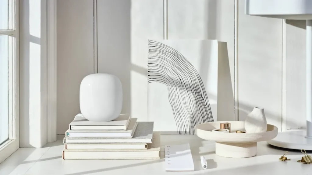 Sleek white Google Nest Wifi Pro mesh router resting on stacked books in a bright, sunlit room.