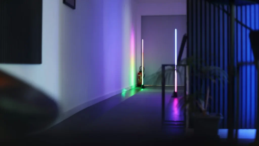 A dark modern hallway split by vertical LED light poles glowing in rainbow colors.