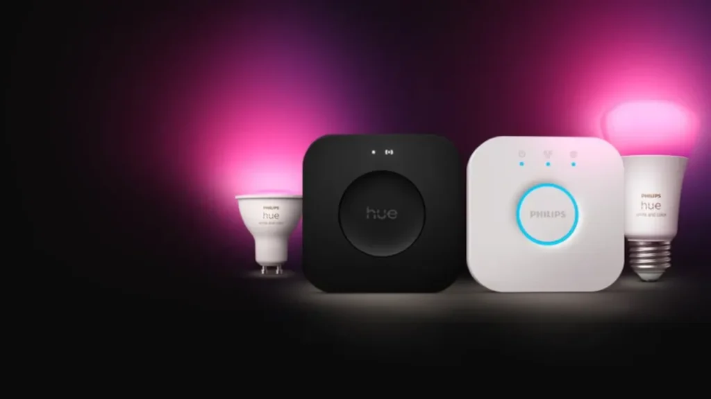 A Philips Hue Bridge, Sync Box, and smart LED bulbs arranged against a colorful background.