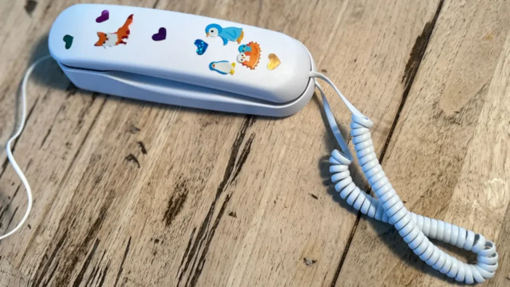 A white Pinwheel Home phone handset on a wooden floor decorated with colorful stickers.