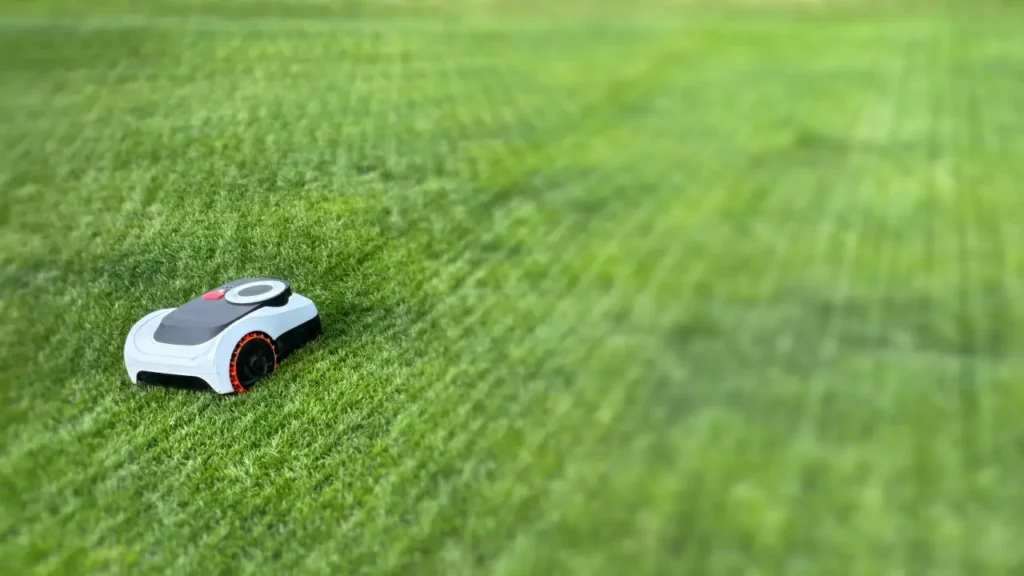 A compact robot mower cutting a large, wide-open grass lawn emphasizing battery capacity.