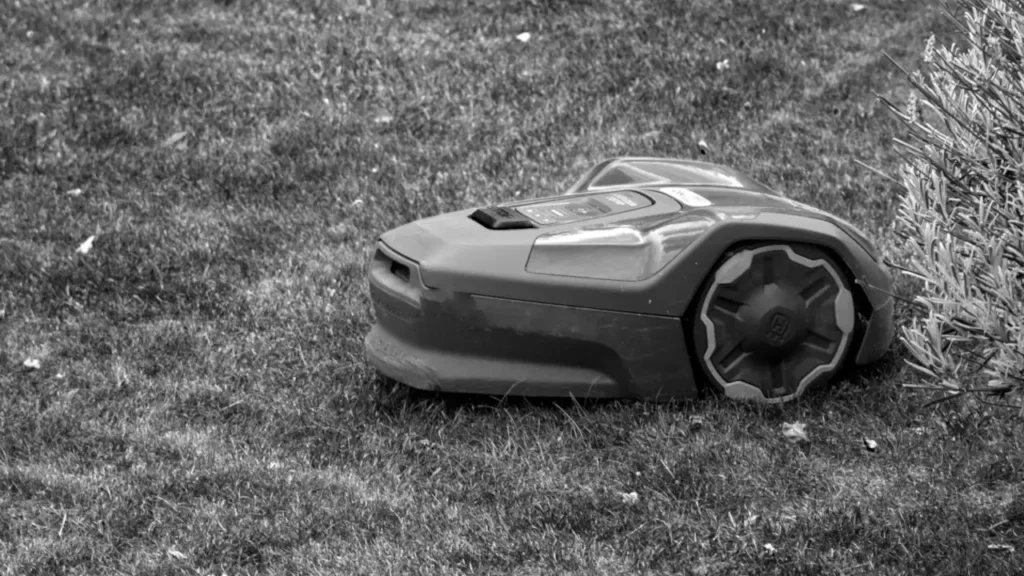Black and white photo of a robotic lawn mower sitting offline in the grass.