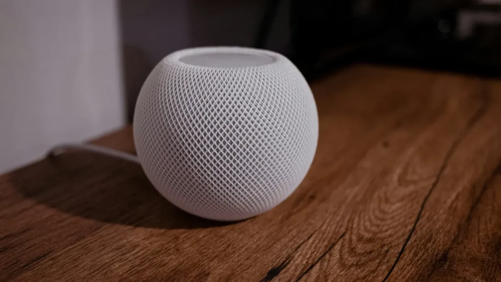 White HomePod Mini smart speaker resting on a textured wooden table.