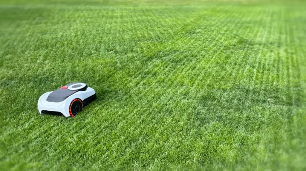 A compact robot mower cutting a large, wide-open grass lawn emphasizing battery capacity.
