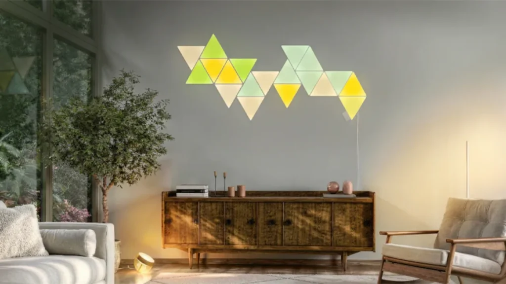 Nanoleaf Shapes triangle panels glowing green and yellow on a living room wall above a wooden sideboard.