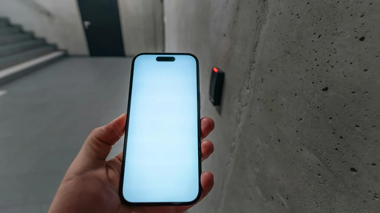 Hand holding a smartphone next to a small NFC reader mounted on a concrete wall