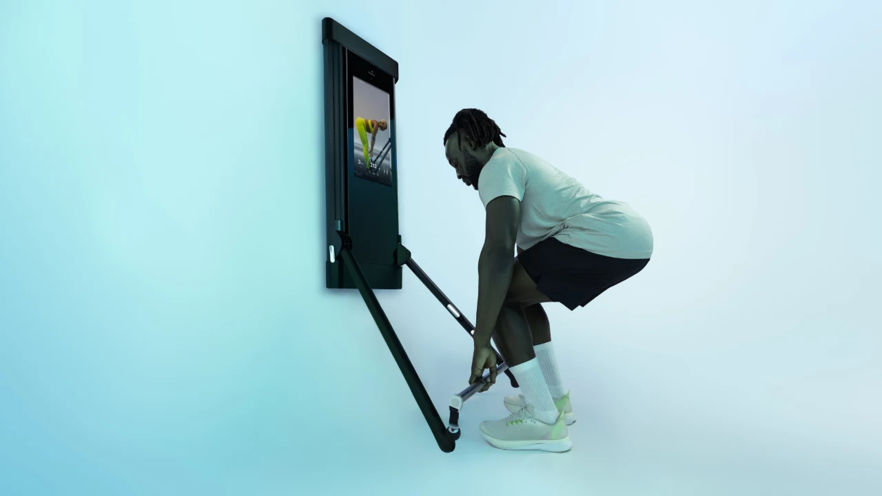Person doing a deadlift with a bar attached to the cable arms of a Tonal 2 wall-mounted gym