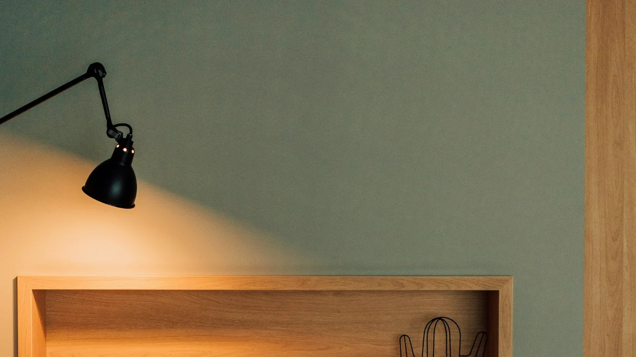 Warm wall lamp glowing above a shelf and sofa in a living room at dusk